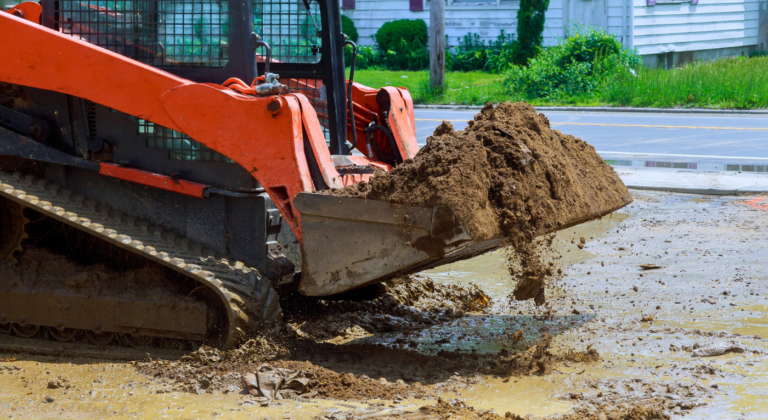 Compact skid steer loader performing grading and dirt removal on a wet, muddy jobsite – Outta Bounds Excavation ensuring site preparation in all conditions."