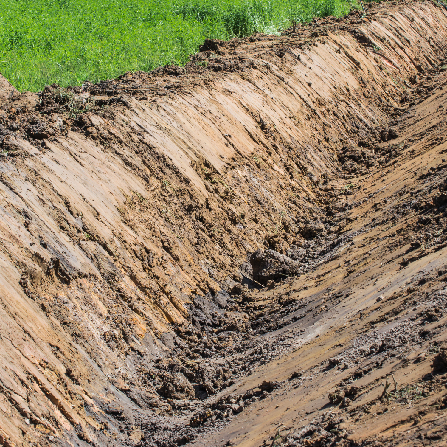 Freshly excavated drainage ditch as part of rough and final grading in Northeast Texas, designed to manage water flow and prevent erosion.
