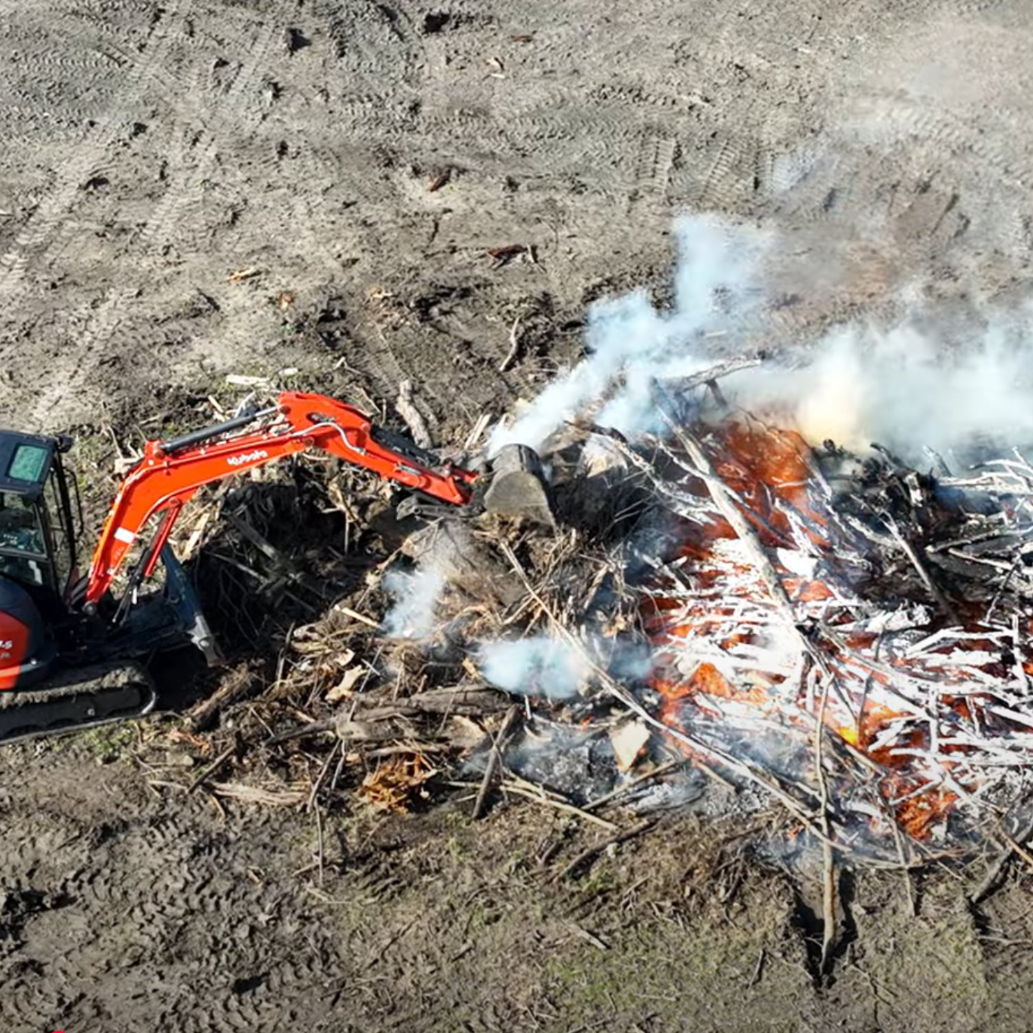Excavation company in North Texas performing land clearing with controlled burn using compact excavator