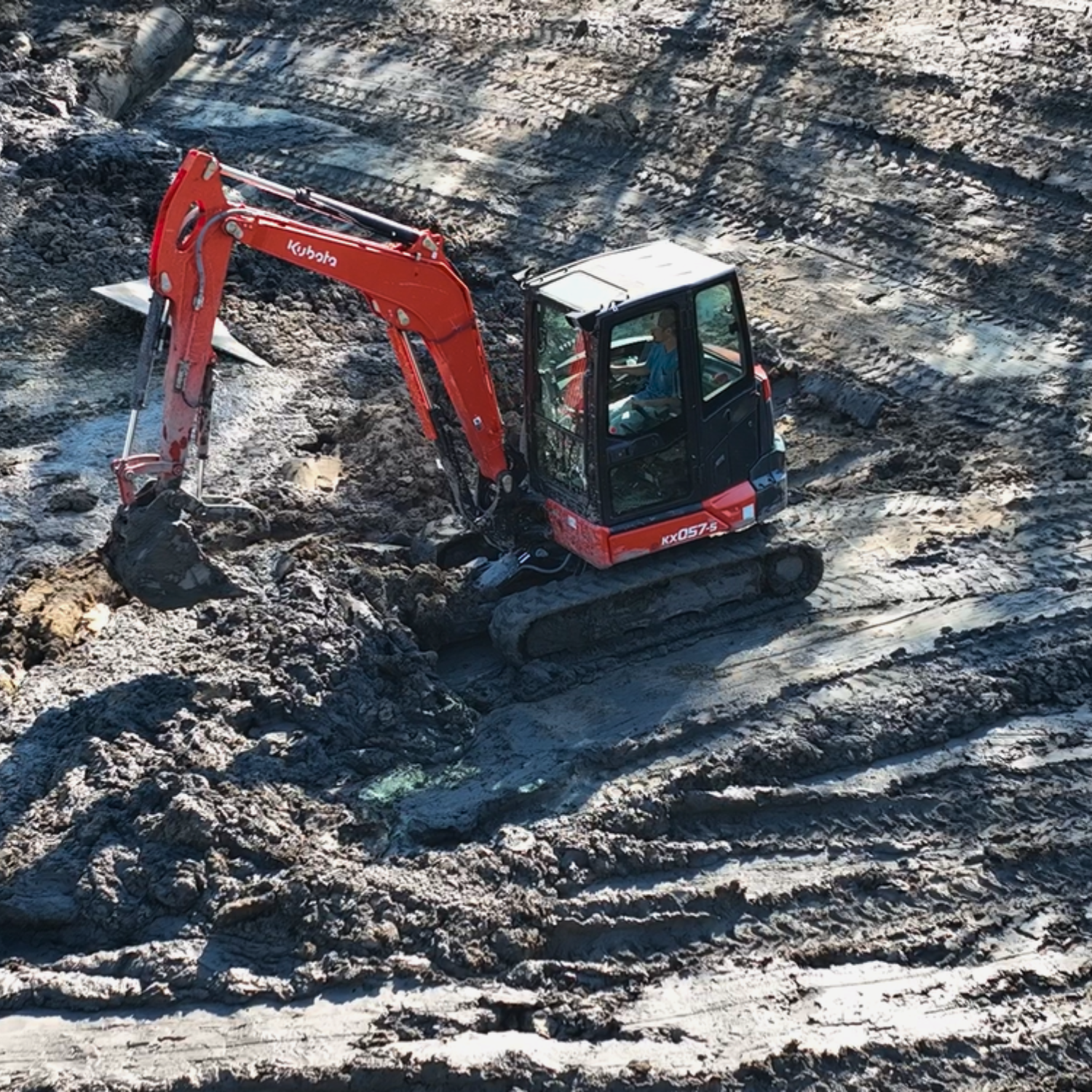 Compact excavator performing pond excavation services on a muddy construction site